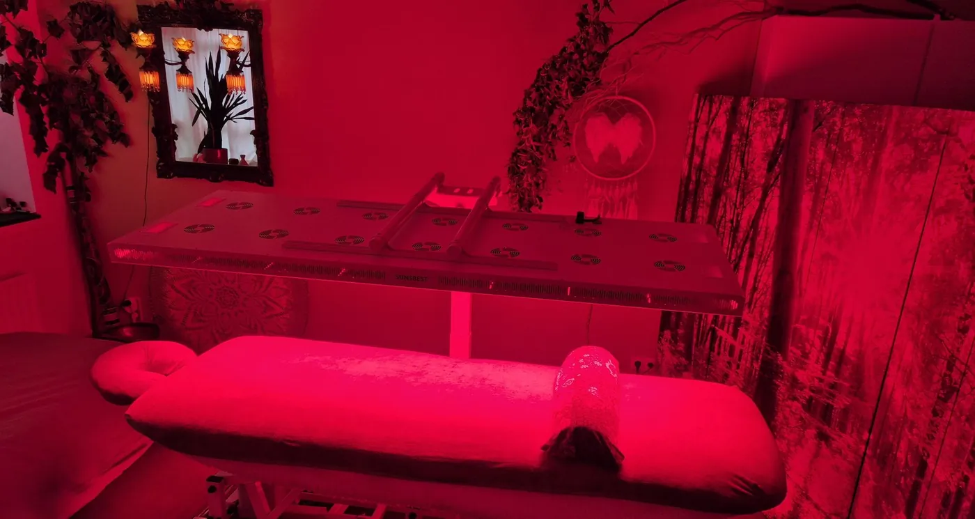 Behandelruimte met rood-lichttherapiepaneel boven de behandeltafel